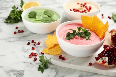 Photo of Bowl of delicious pink hummus with tortilla chips and parsley on white marble table