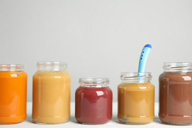 Healthy baby food in jars on white wooden table against grey background, space for text