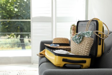 Open suitcase full of clothes, shoes and summer accessories on sofa in room. Space for text