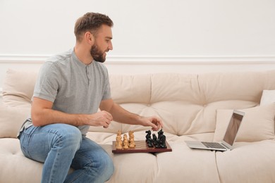 Photo of Young man playing chess with partner through online video chat at home