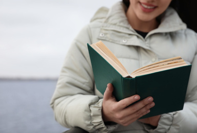 Photo of Woman reading book near river on cloudy day, closeup