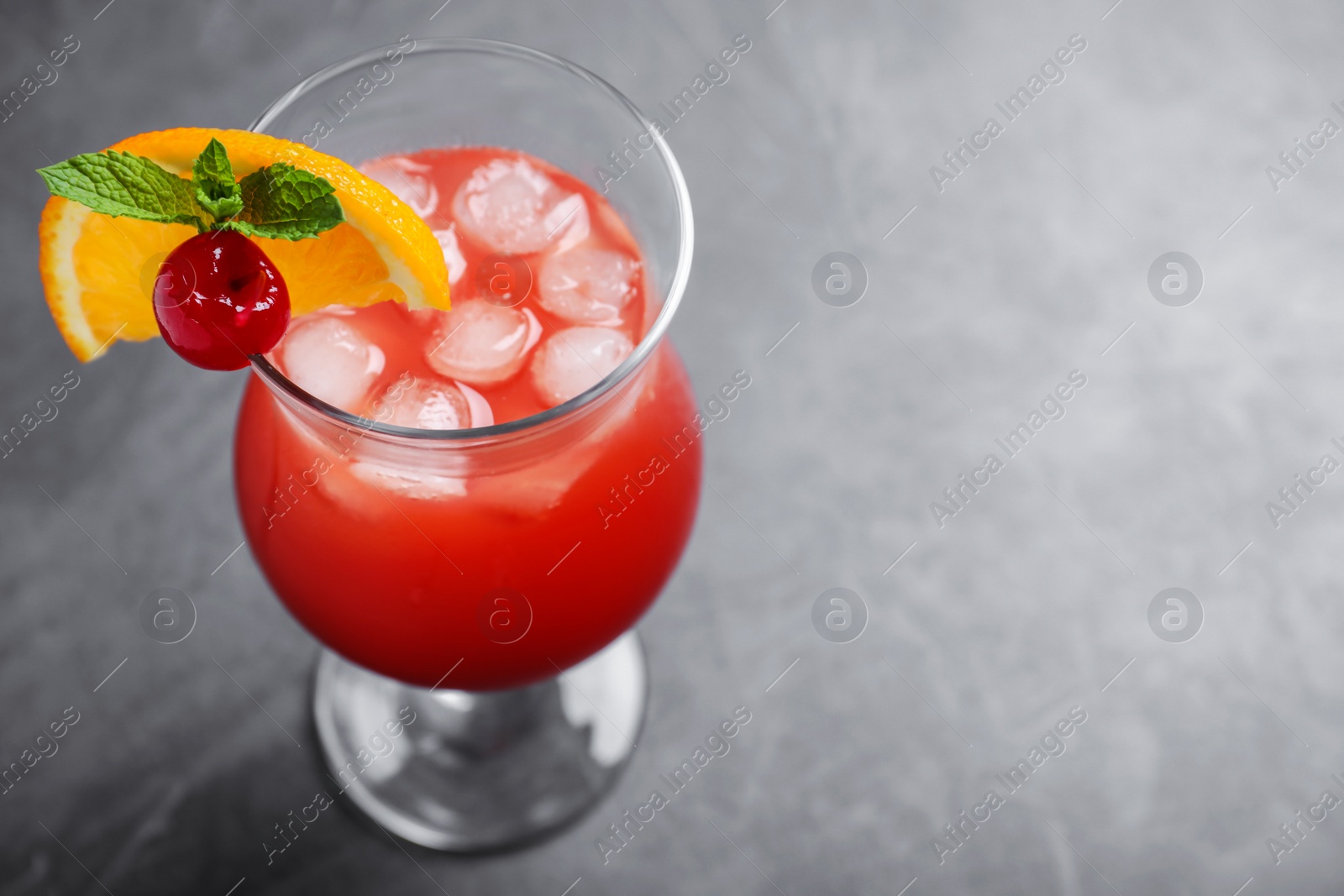 Photo of Glass of tasty refreshing cocktail on grey table. Space for text