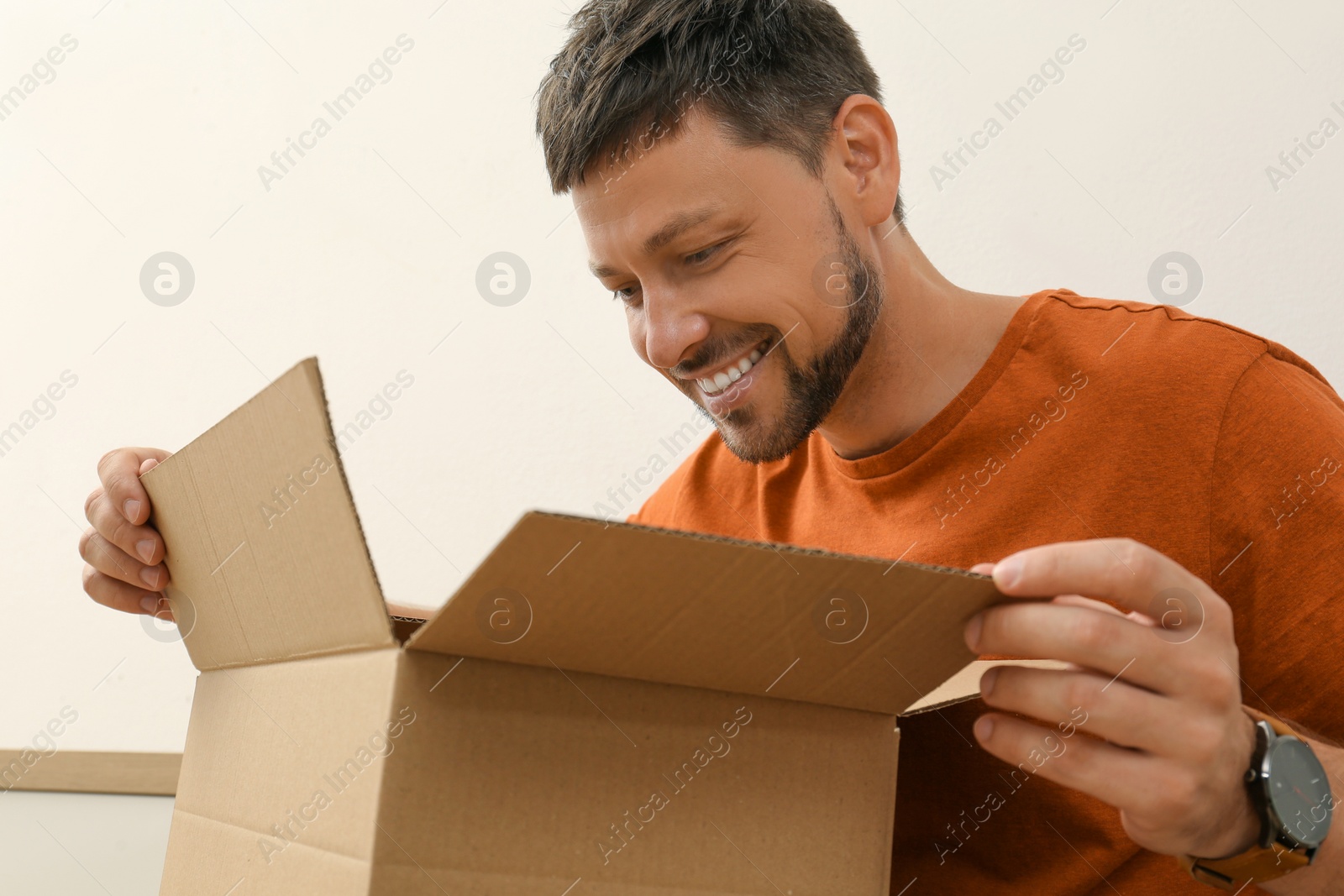 Photo of Happy man opening parcel indoors. Internet shopping