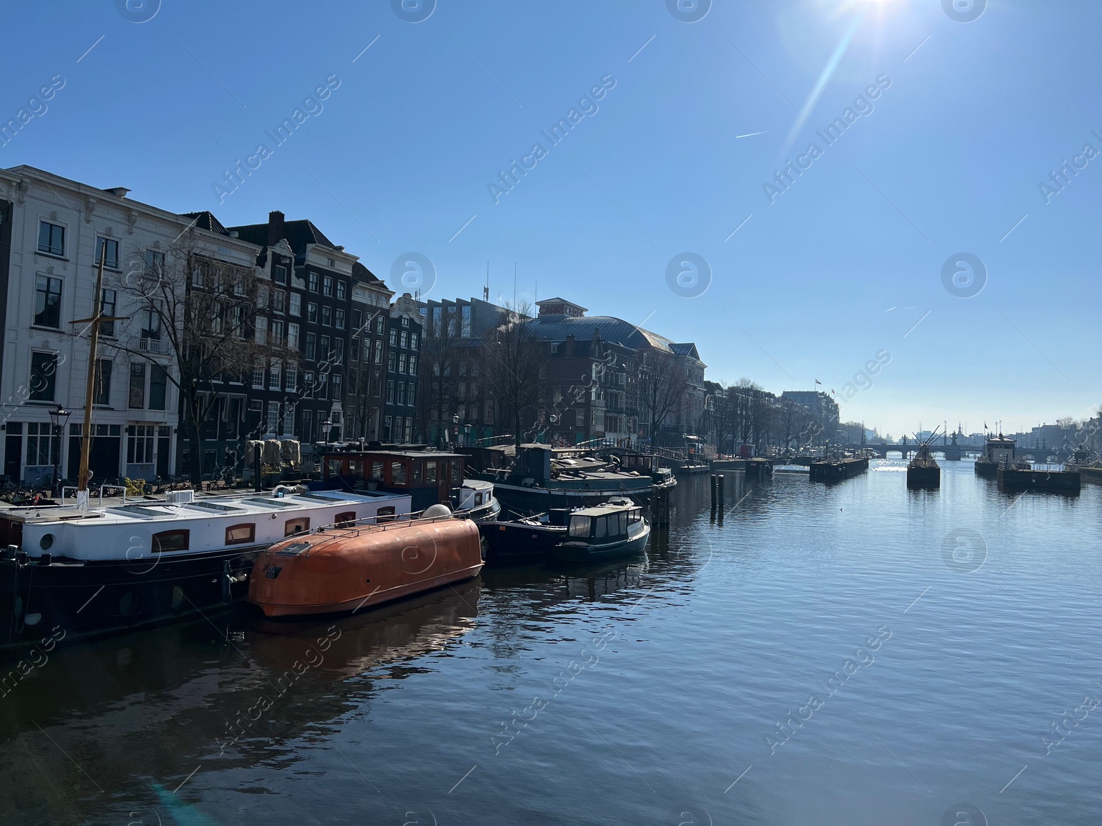 Photo of Amsterdam, Netherlands - March 01, 2023: Picturesque view of river embankment with moored boats in city under blue sky