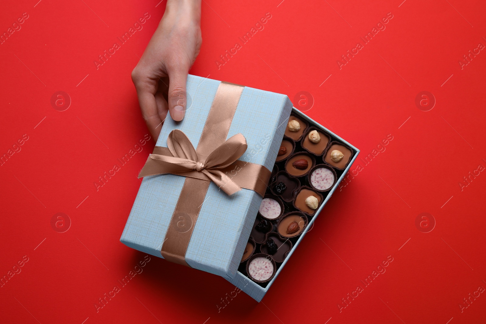 Photo of Woman with open box of delicious chocolate candies on red background, top view