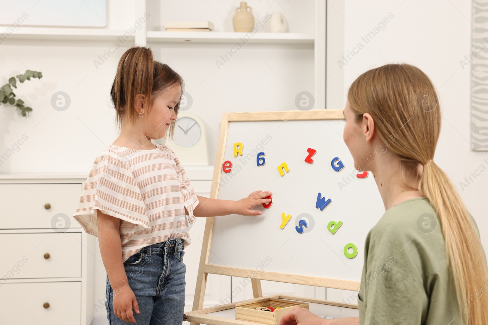 Photo of Mom teaching her daughter alphabet with magnetic letters at home