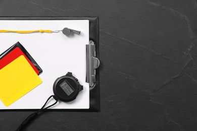 Photo of Referee equipment. Whistle, clipboard, cards and stopwatch on black table, top view with space for text