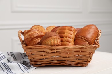 Photo of Wicker basket with different tasty freshly baked pastries on white wooden table, closeup