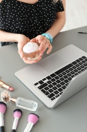 Photo of Young woman with makeup products using laptop at table. Beauty blogger