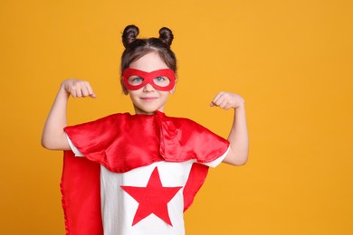 Photo of Cute little girl in superhero suit on yellow background. Space for text