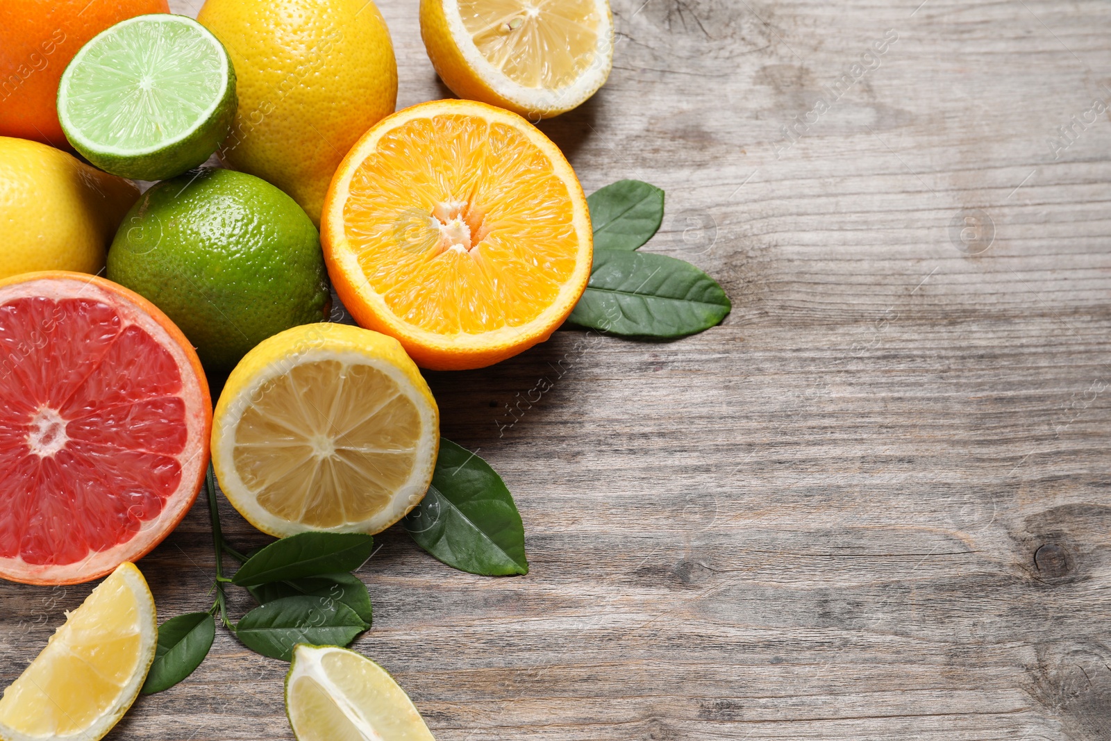 Photo of Different fresh citrus fruits and leaves on wooden table, flat lay. Space for text