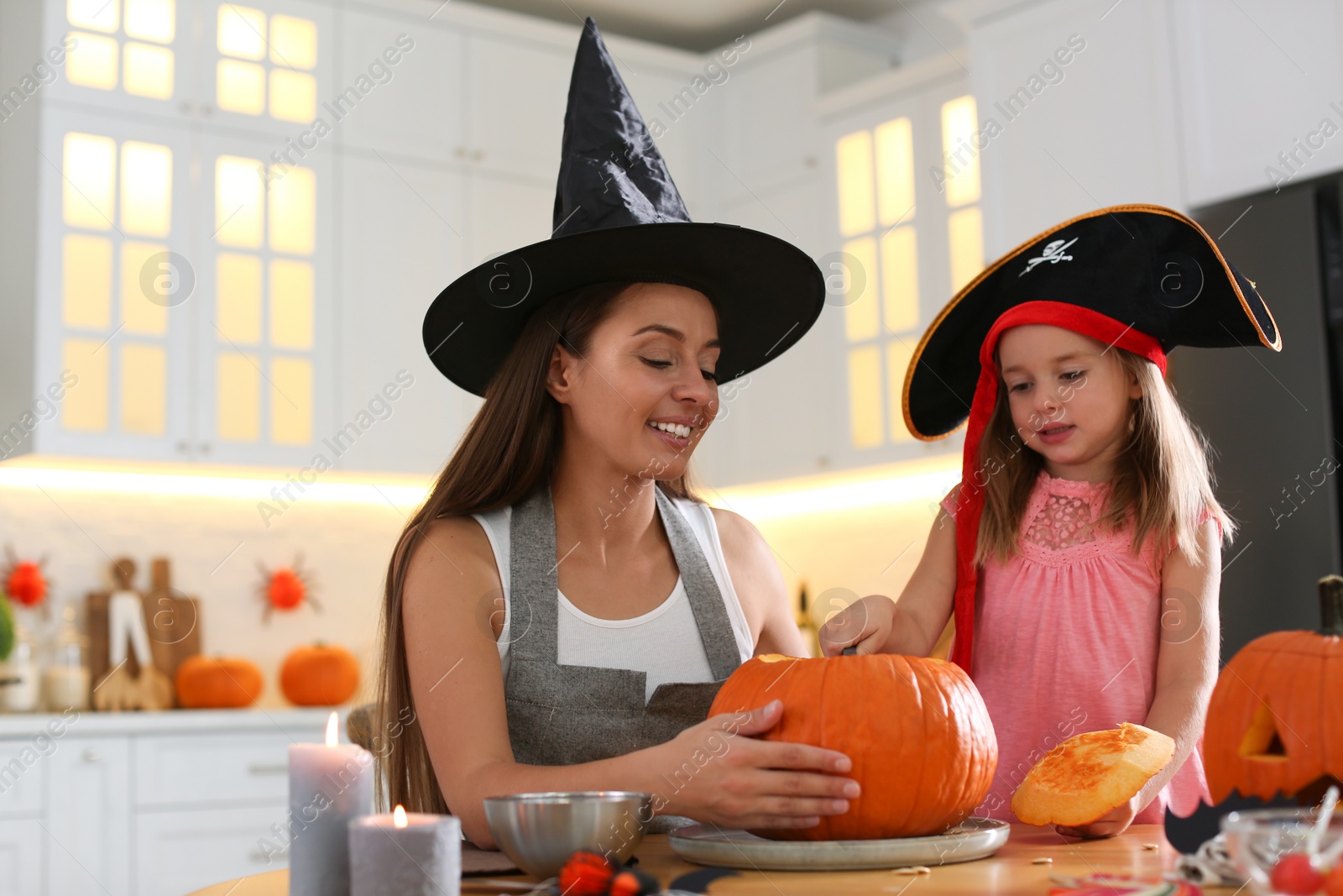 Photo of Mother and daughter making pumpkin jack o'lantern at table in kitchen. Halloween celebration