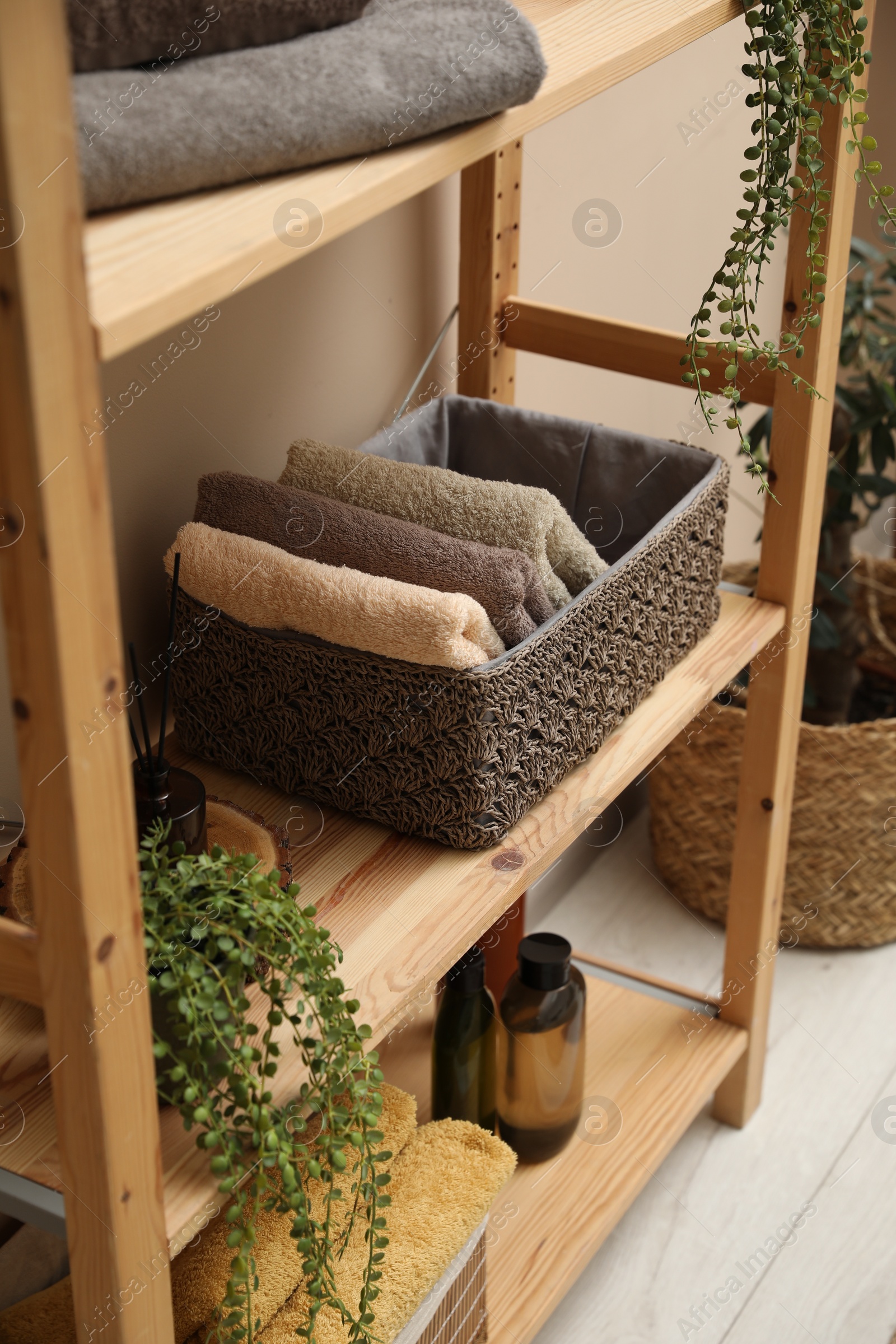 Photo of Soft towels in storage boxes, plant and bottles on shelves indoors