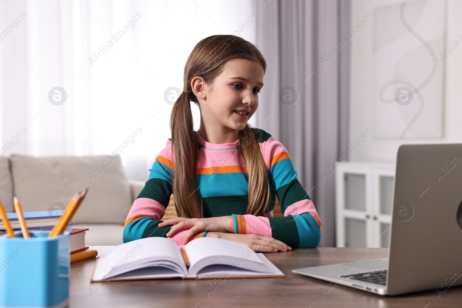 Photo of E-learning. Cute girl using laptop during online lesson at table indoors