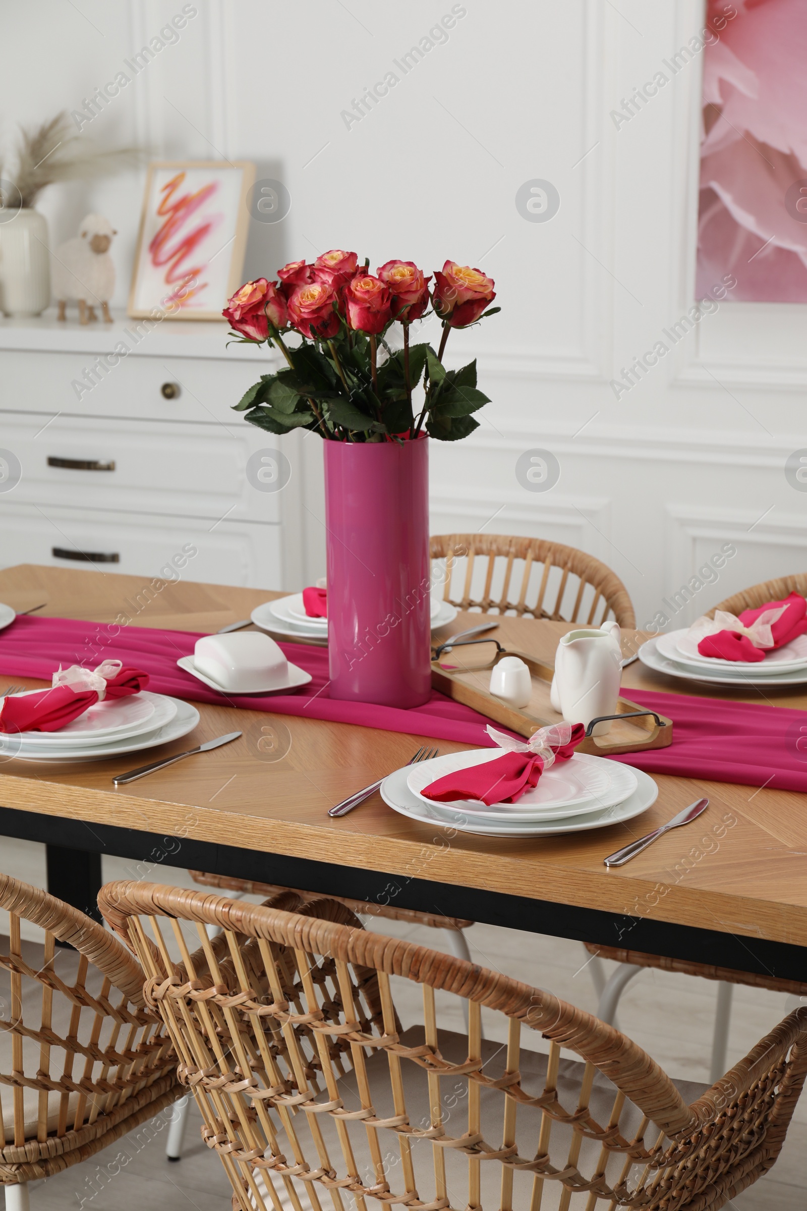 Photo of Color accent table setting. Plates, cutlery, pink napkins and vase with beautiful roses in dining room