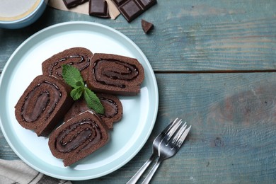 Photo of Tasty chocolate cake roll with cream and mint on blue wooden table, flat lay. Space for text