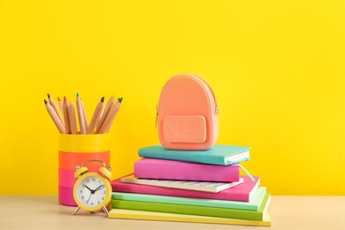 Photo of Different school stationery and alarm clock on table against yellow background. Back to school