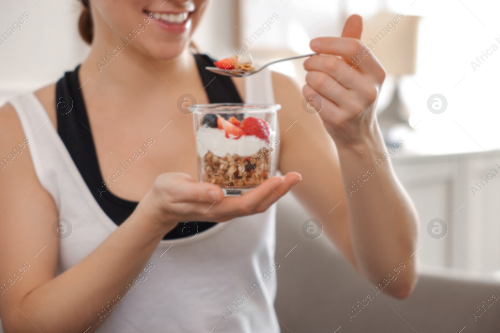 Photo of Woman eating tasty granola with fresh berries and yogurt at home, closeup