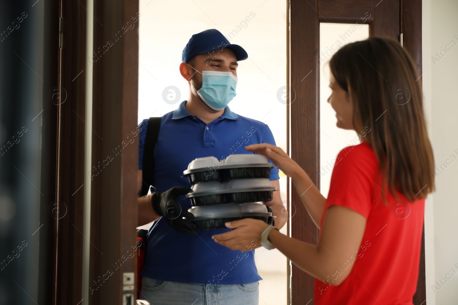 Photo of Courier in protective mask and gloves giving order to woman at entrance. Restaurant delivery service during coronavirus quarantine