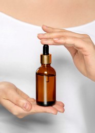 Woman holding bottle of essential oil on white background, closeup