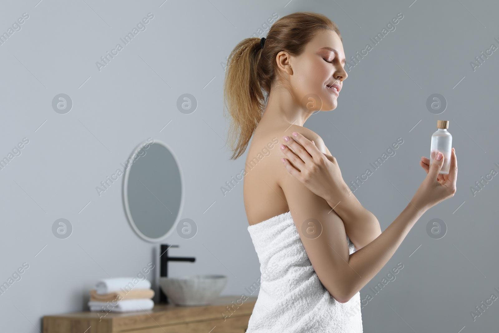 Photo of Beautiful woman applying body oil onto shoulder in bathroom, space for text