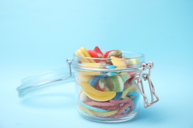 Photo of Tasty colorful jelly candies in glass jar on light blue background, closeup