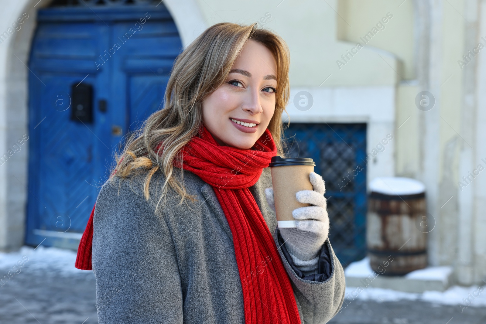 Photo of Portrait of smiling woman with paper cup of coffee on city street in winter