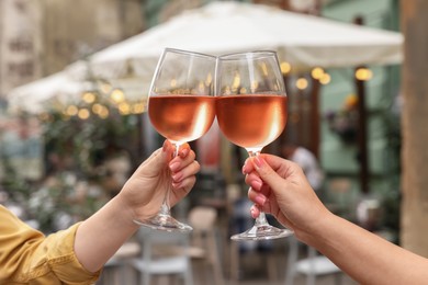 Photo of Women clinking glasses with rose wine outdoors, closeup