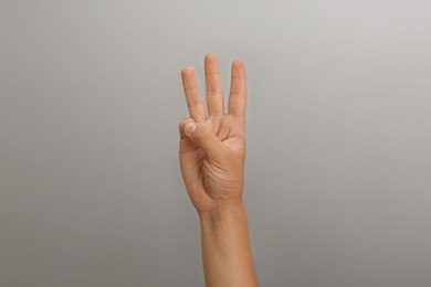 Photo of Teenage boy showing three fingers on light grey background, closeup