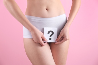 Young woman holding paper with question mark near underwear on color background. Gynecology