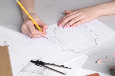 Woman creating packaging design at light wooden table, closeup