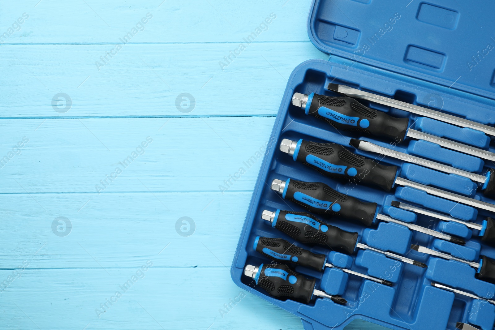 Photo of Set of screwdrivers in open toolbox on light blue wooden table, top view. Space for text