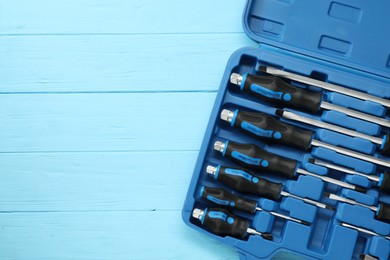 Photo of Set of screwdrivers in open toolbox on light blue wooden table, top view. Space for text
