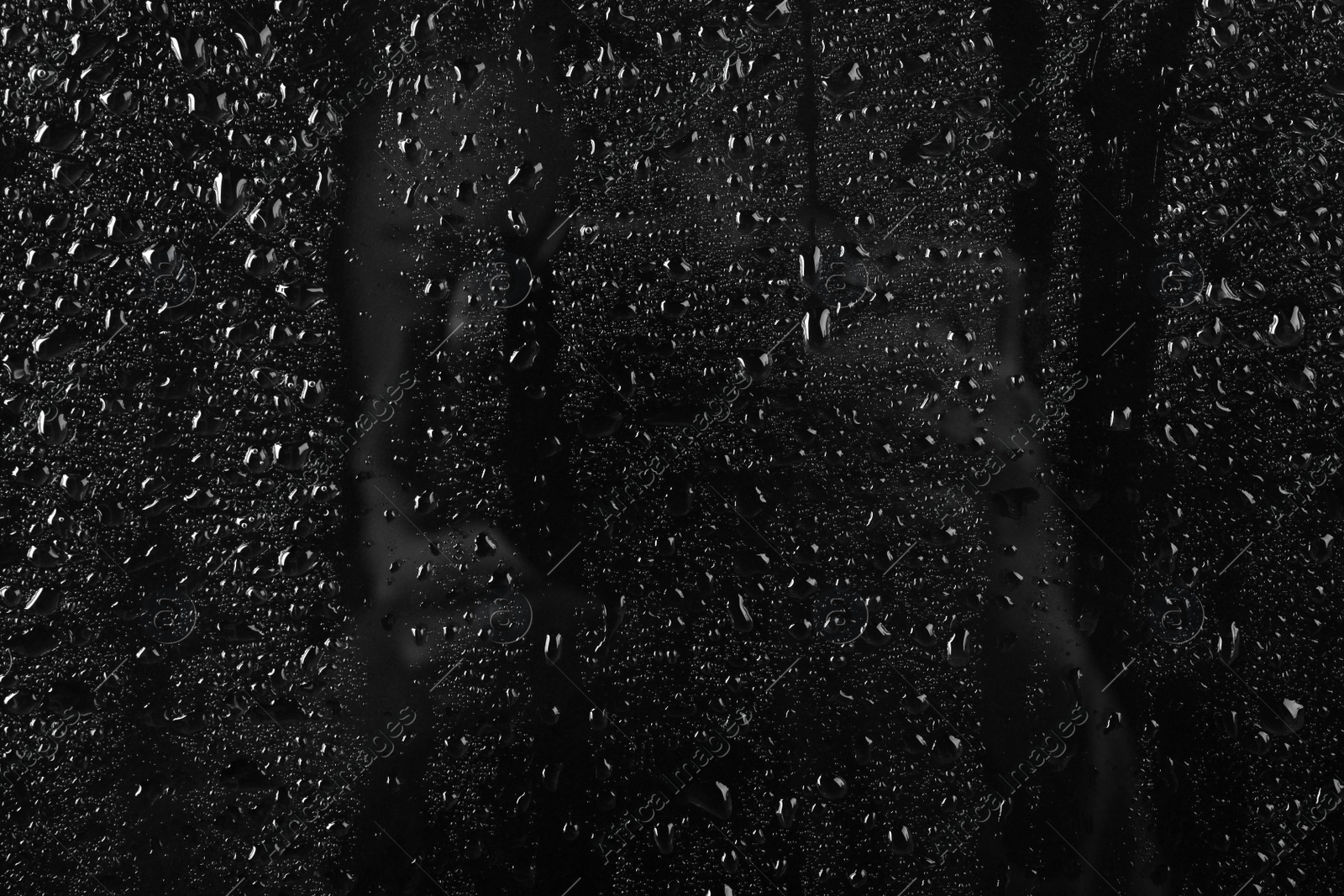 Photo of Glass with rain drops against dark background