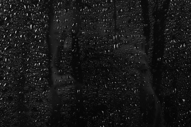 Photo of Glass with rain drops against dark background