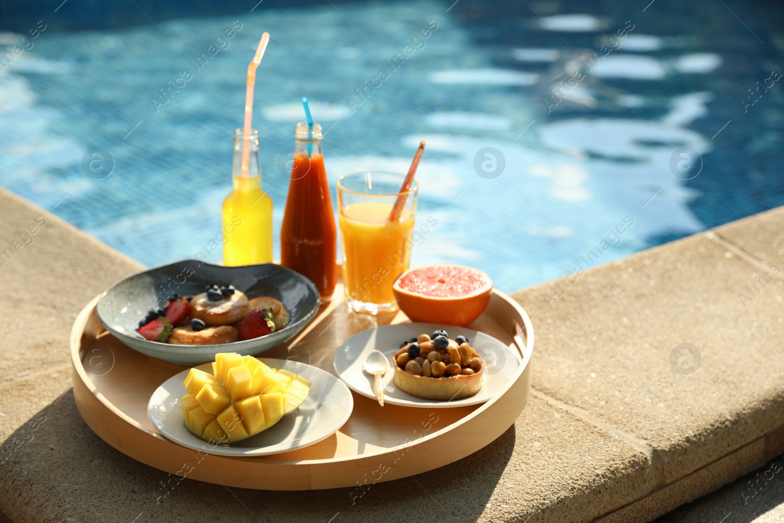 Photo of Tray with delicious breakfast near swimming pool