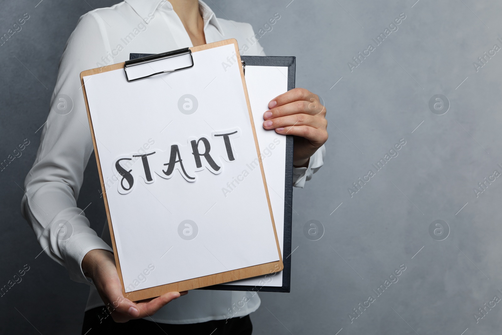 Photo of Woman holding clipboards with word Start on grey background, closeup. Space for text