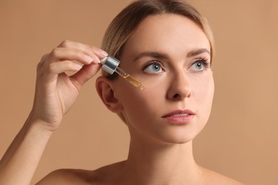 Photo of Beautiful woman applying cosmetic serum onto her face on beige background, closeup