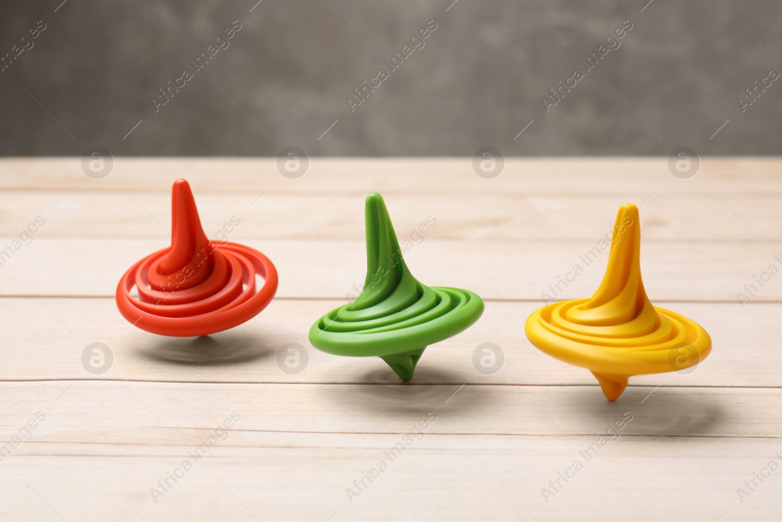 Photo of Bright spinning tops on light wooden table, closeup