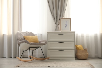 Rocking chair and chest of drawers near window with stylish curtains in living room. Interior design