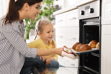 Photo of Mother and daughter taking out buns from oven in kitchen