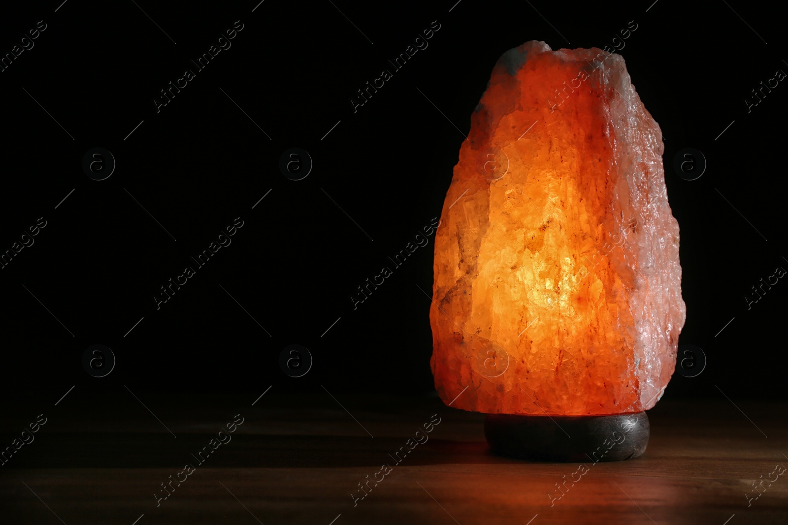 Photo of Himalayan salt lamp on table against black background. Space for text