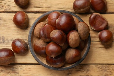 Photo of Sweet fresh edible chestnuts in bowl on wooden table, top view