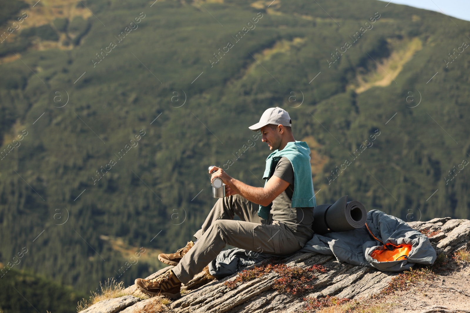 Photo of Tourist with hot drink, sleeping bag and mat on mountain peak