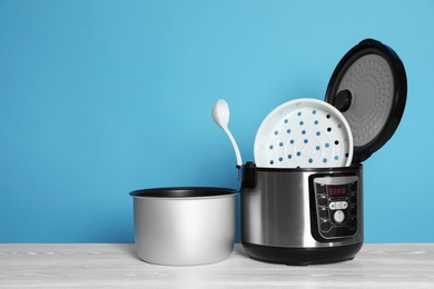 Photo of Disassembled electric multi cooker with spoon on table against color background. Space for text