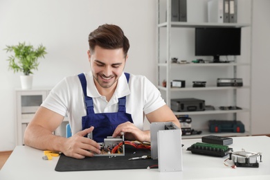 Male technician repairing power supply unit at table indoors