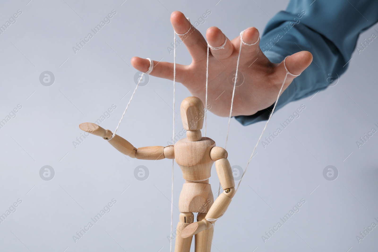 Photo of Woman pulling strings of puppet on light grey background, closeup