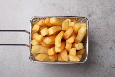 Frying basket with tasty french fries on light grey table, top view