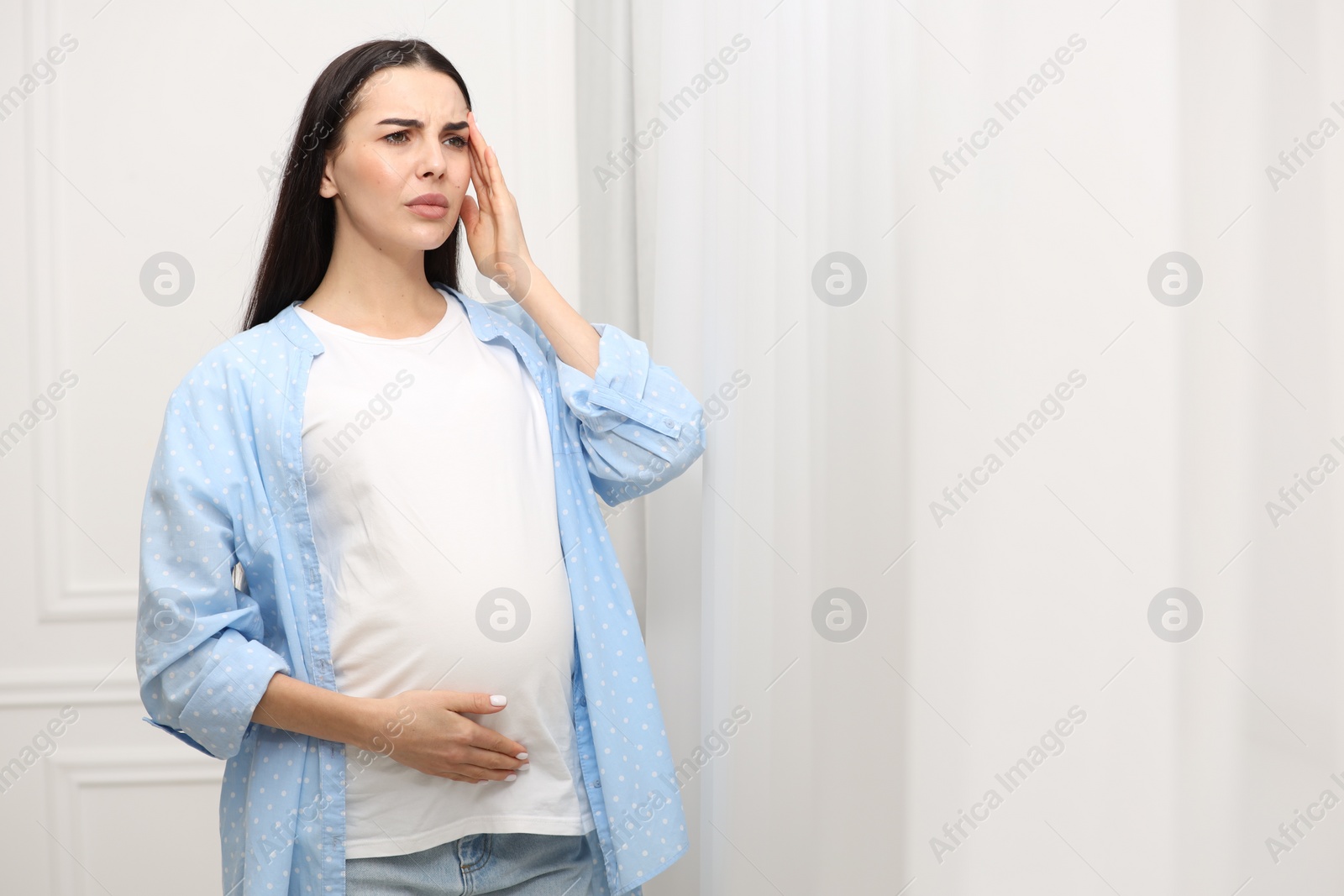 Photo of Pregnant woman suffering from headache indoors, space for text