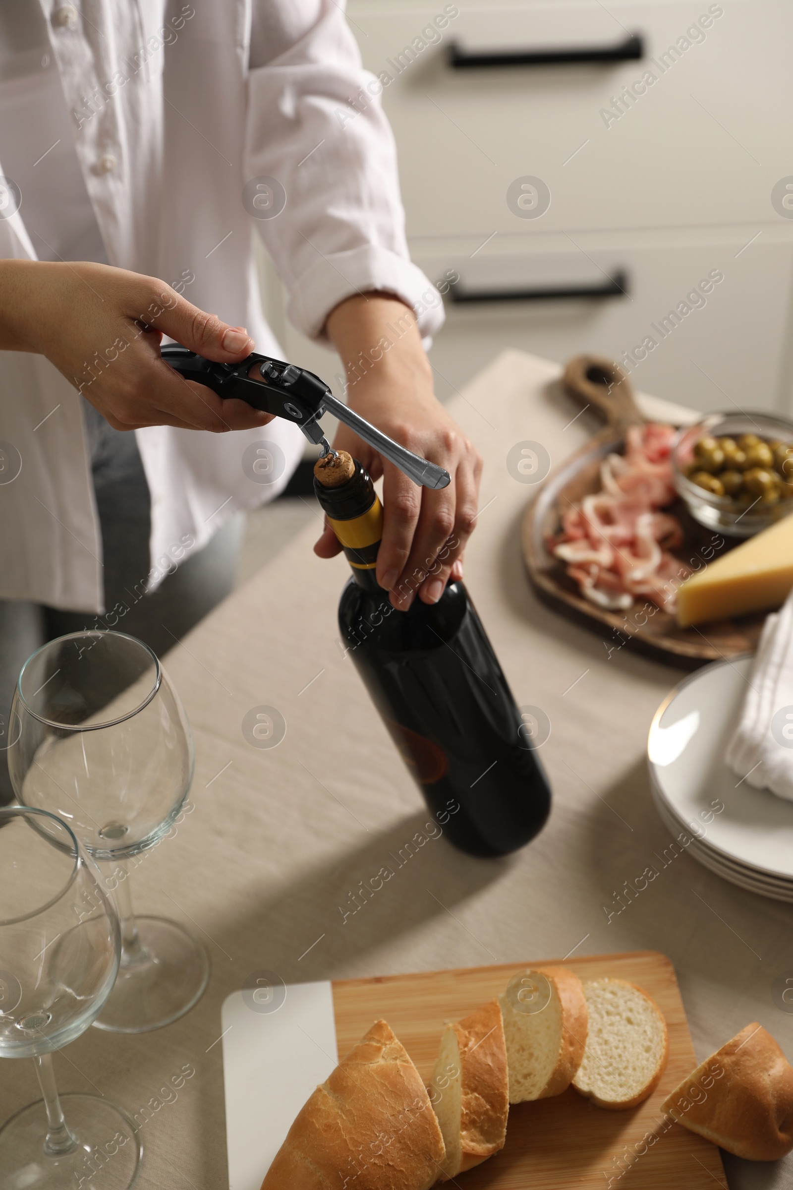 Photo of Woman opening wine bottle with corkscrew at table indoors, closeup